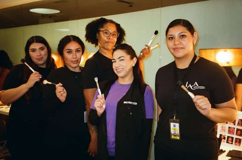 Group photo of LACA students and instructors holding makeup brushes